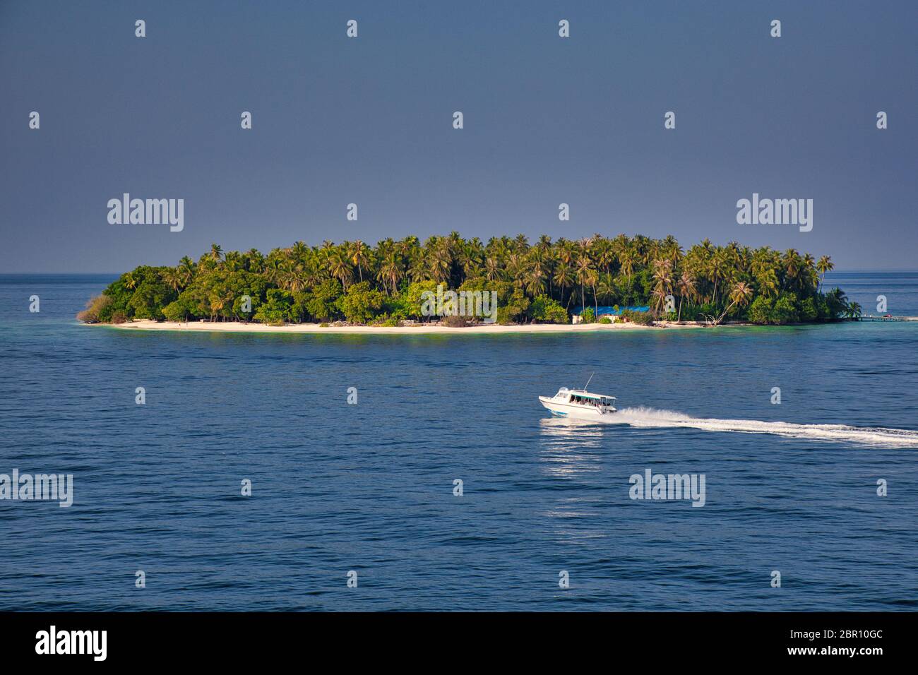 Kuda Bandos, eine typische maledivische Wüsteninsel im Indischen Ozean mit einem blauen azurblauen Meer im Vordergrund und einem Schnellboot, das durchfährt Stockfoto