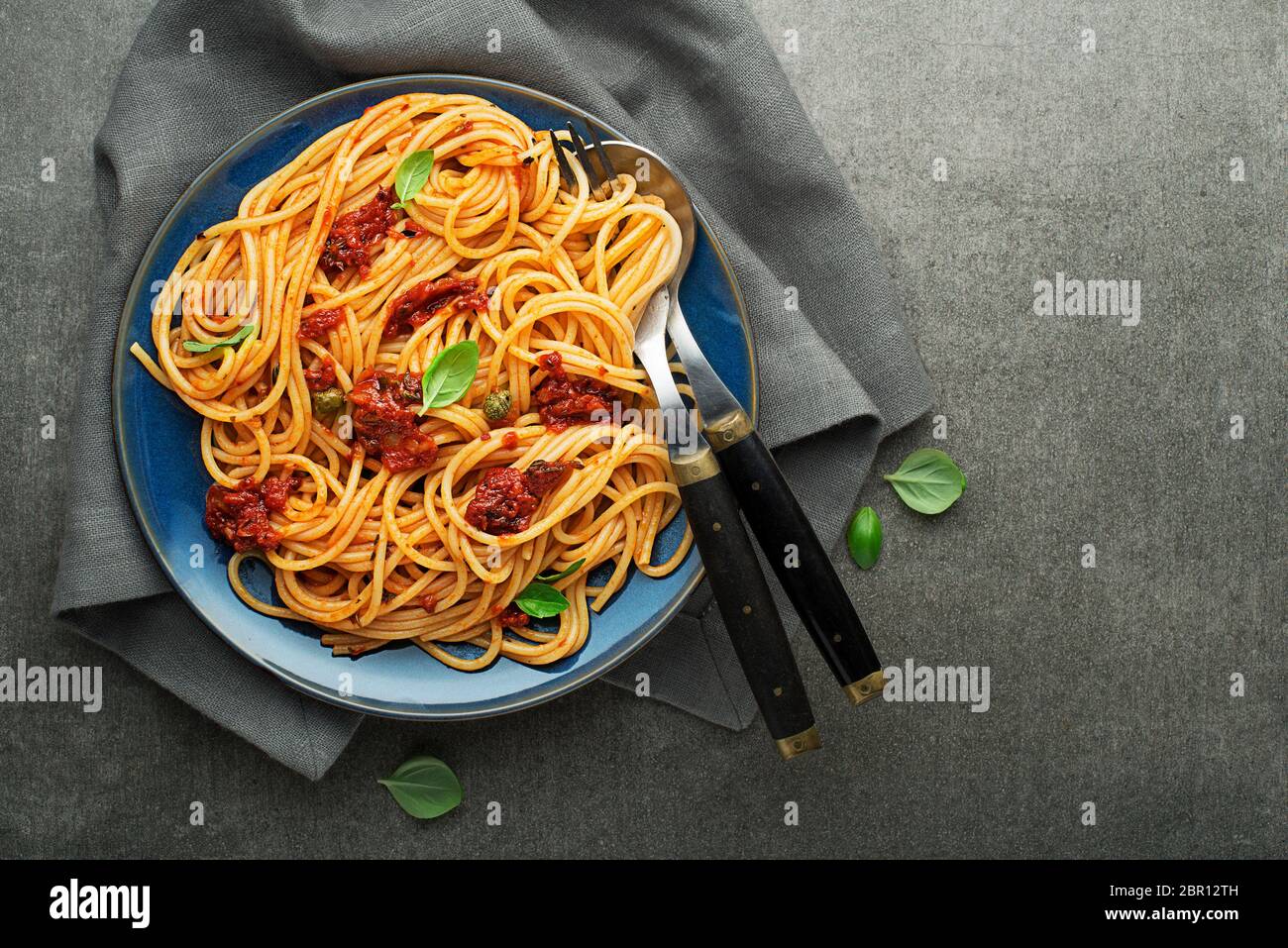 Köstliche Mahlzeit mit Spaghetti und Tomatensauce mit Basilikum auf grauem Hintergrund serviert. Stockfoto