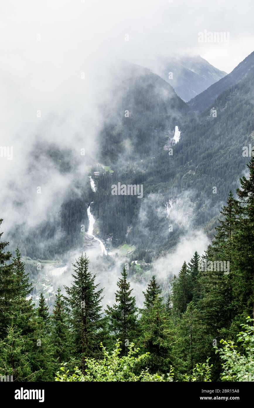 Fernsicht der Krimmler Wasserfälle zwischen Bäumen an einem trüben und nebligen Tag in Österreich. Höchster Wasserfall in europa Stockfoto