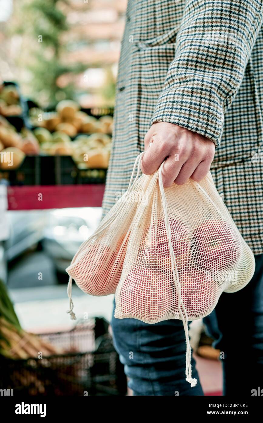 Nahaufnahme eines Mannes, Einkaufen in einem Gemüsehändler oder einem Straßenmarkt, mit einigen textilen wiederverwendbaren Netztüten voller Obst und Gemüse, als Maßnahme zu rot Stockfoto