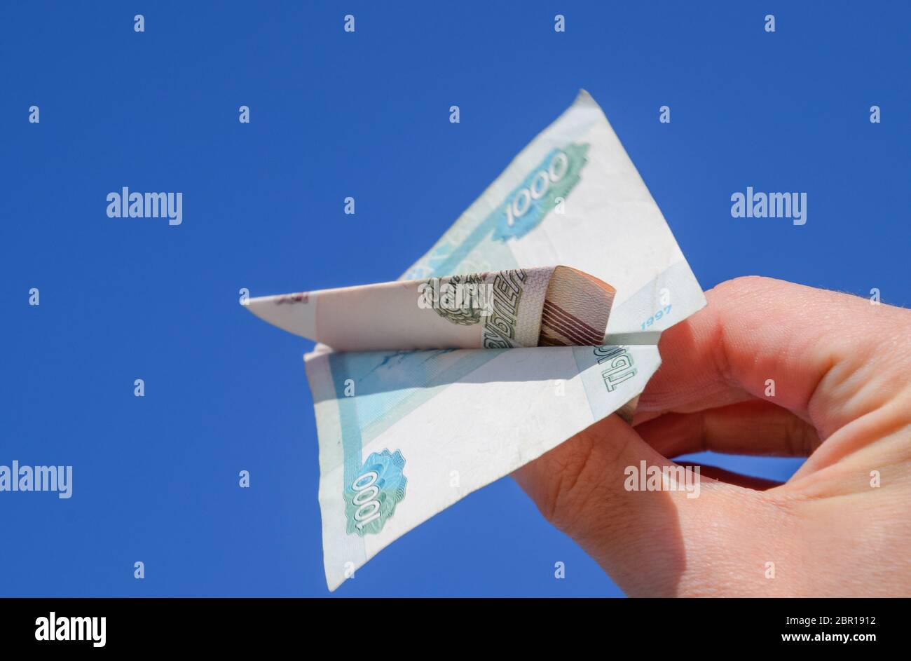 Stückelung der russischen Geld, gefaltet in das Flugzeug gegen den blauen Himmel in der hand. Stockfoto