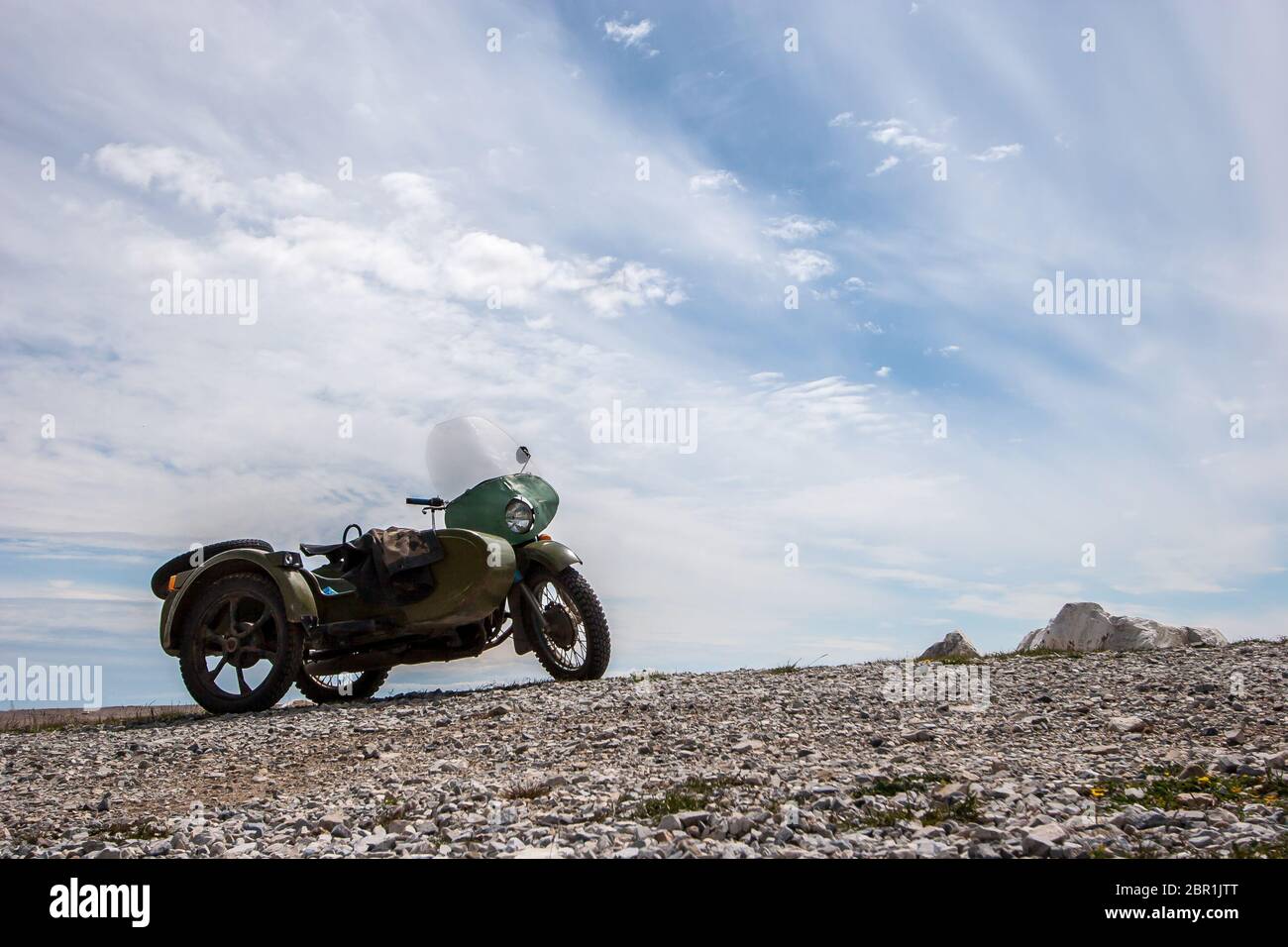 Ein altes sowjetisches Motorrad mit Seitenwagen steht gegen den Himmel mit Wolken auf den Steinen. Grüne Farbe. Windschutzscheibe und runder Scheinwerfer. Horizontal. Stockfoto