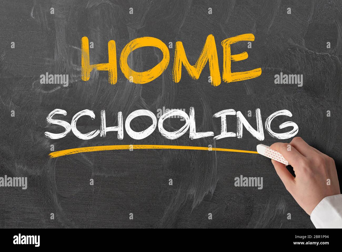Hand hält Stück Kreide gegen Tafel mit Text HOME SCHULE, Bildung während Covid-19 Coronavirus Sperrung Stockfoto