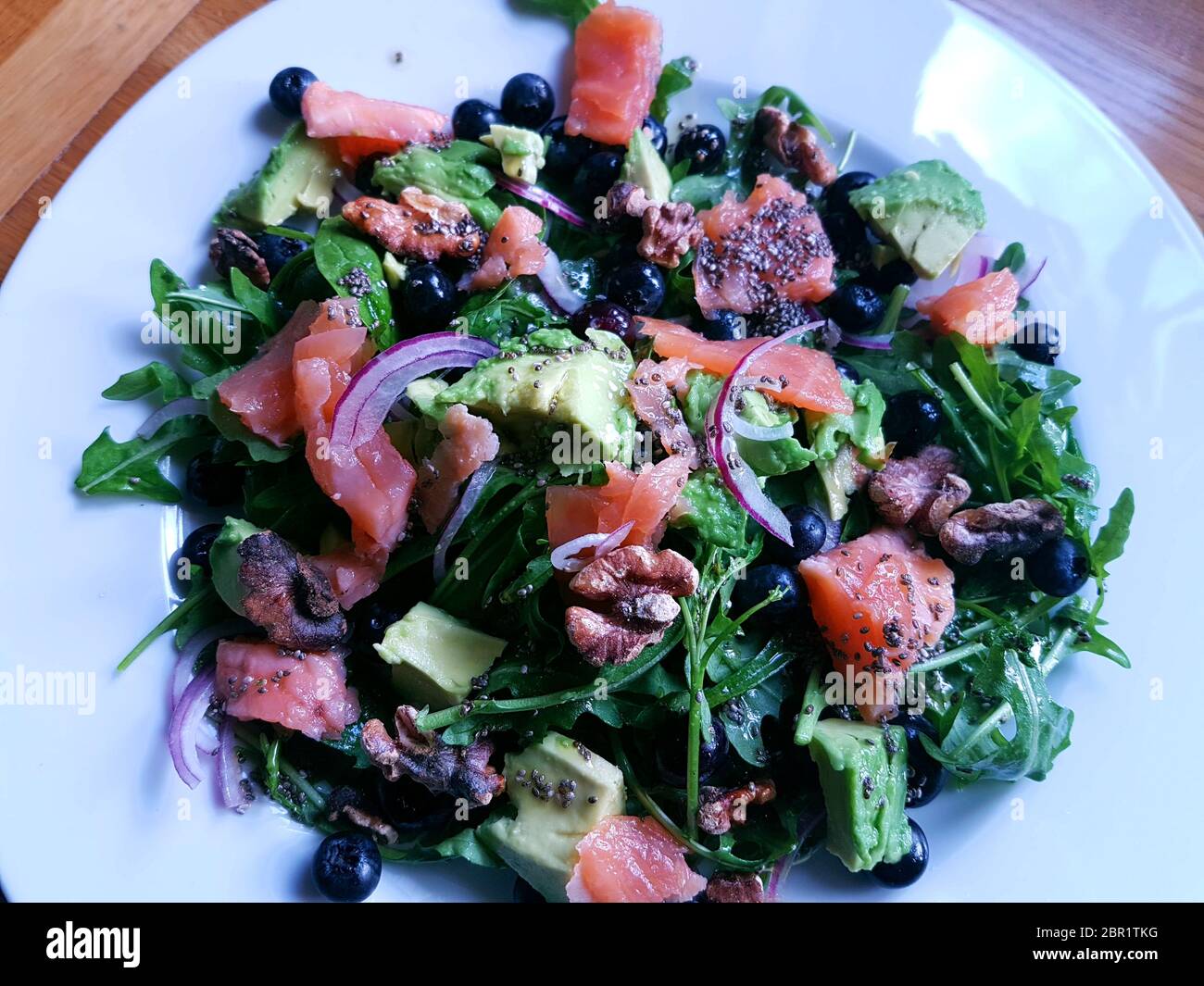 Heißer geräucherter Lachs mit Heidelbeeren, Rucola und Avocado auf einem weißen Teller Stockfoto