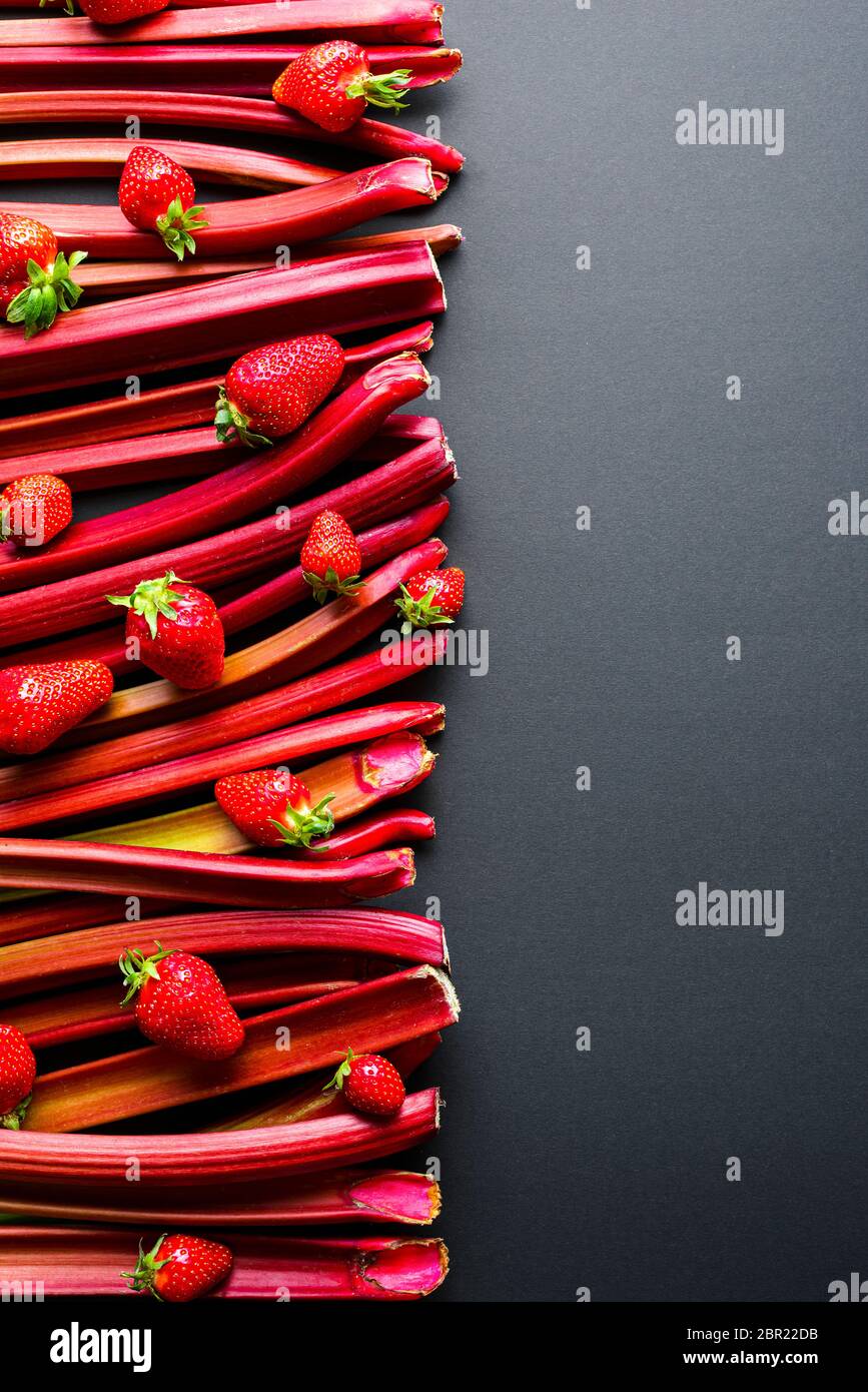 Erdbeeren und Rhabarberstiele auf einem schwarzen Tisch, oben gesehen. Frisches Gemüse und Obst, Zutaten für einen Kuchen Stockfoto