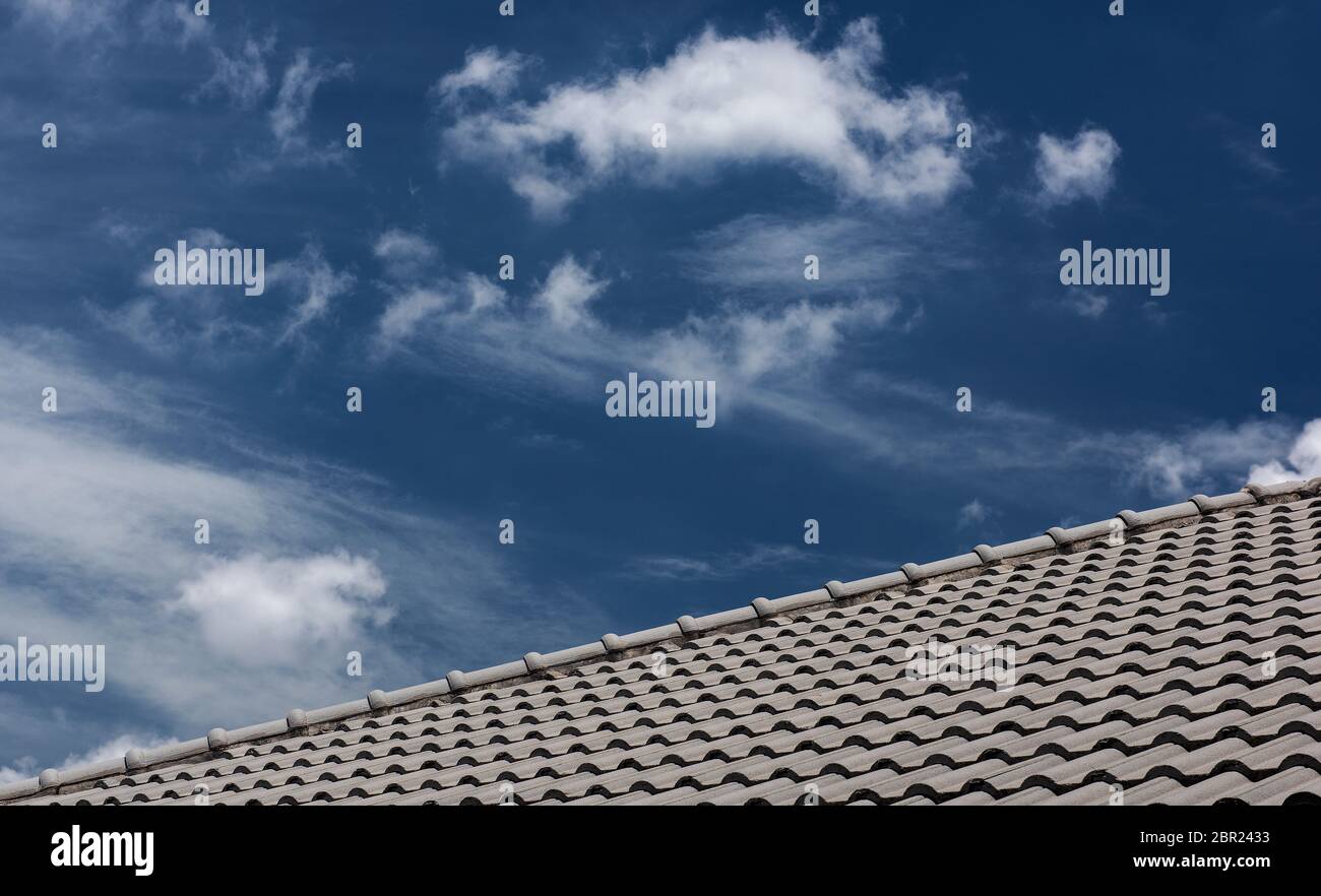 Dach vor blauem Himmel, graues Ziegeldach des Bauhauses mit blauem Himmel und Wolkenhintergrund Stockfoto