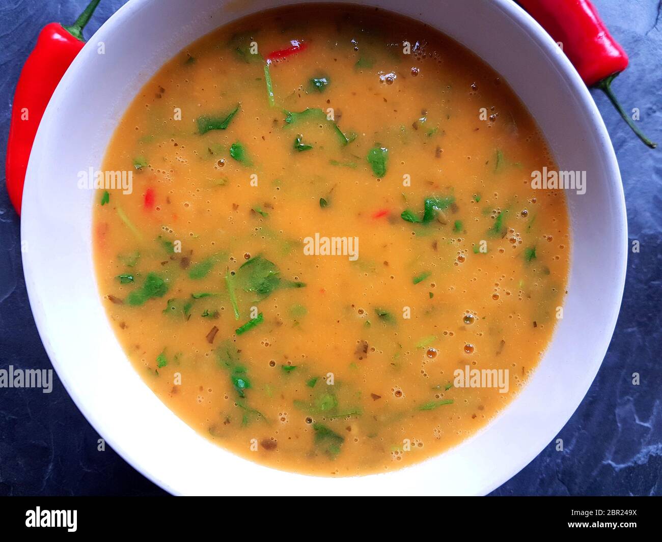 Rote Thai Hühnersuppe in einer weißen Schüssel mit roten Chilis auf Hintergrund Stockfoto