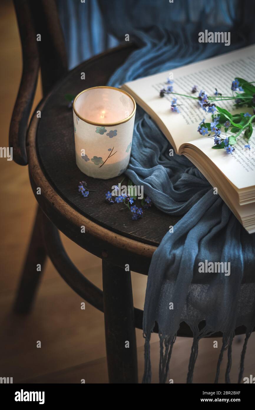 Gemütlicher Moment mit einer Kerze, einem Buch und vergessen Sie mich nicht Blumen auf einem Stuhl Stockfoto