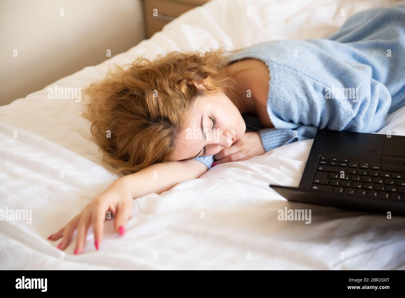 Frau in blauem Pullover mit Laptop im Bett liegend. Stockfoto