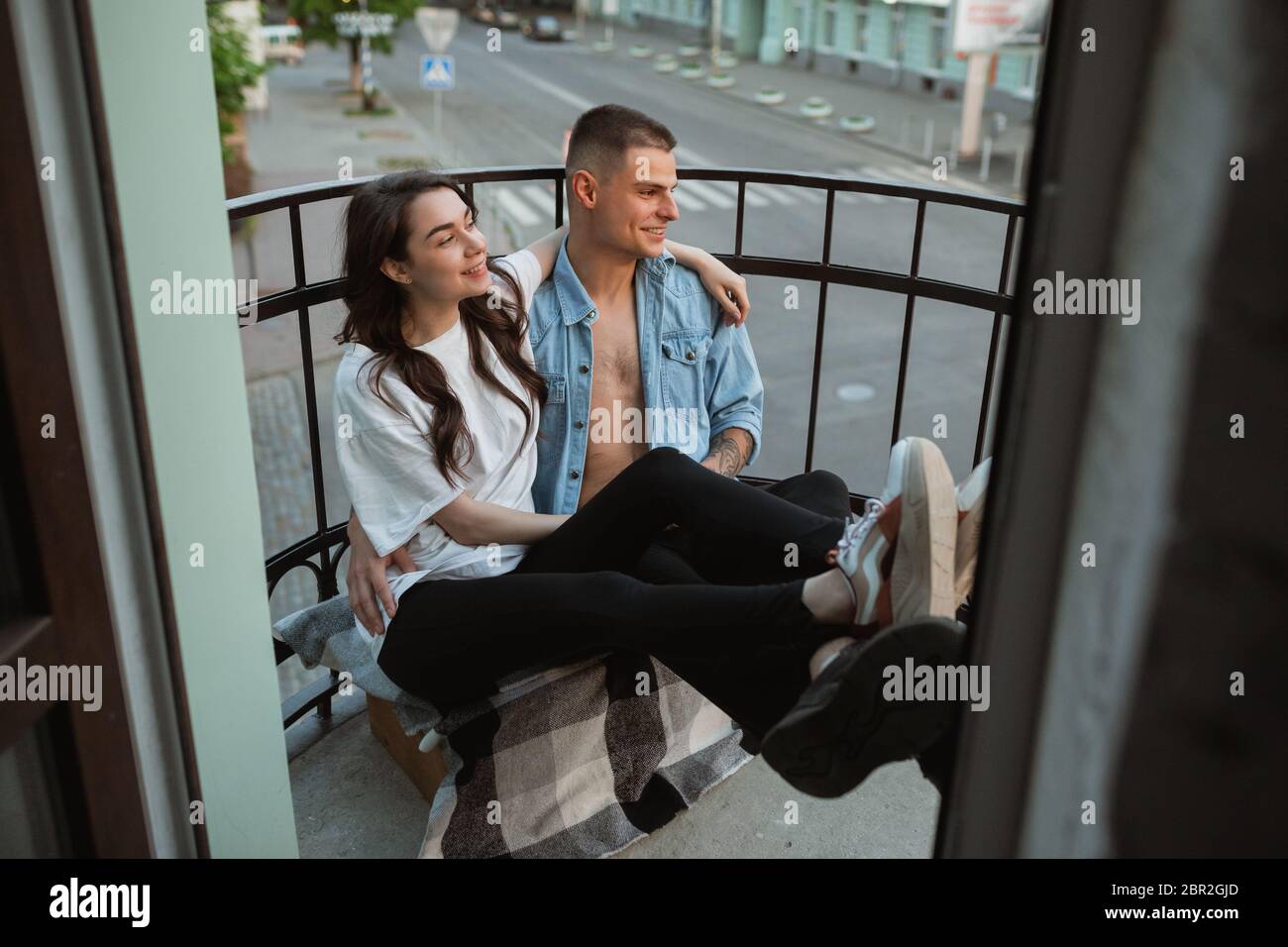 Auf dem Balkon sitzend, lachend. Quarantäne sperren, bleiben zu Hause Konzept - junge schöne kaukasische Paar genießen neuen Lebensstil während Coronavirus. Glück, Zusammengehörigkeit, Gesundheit. Stockfoto