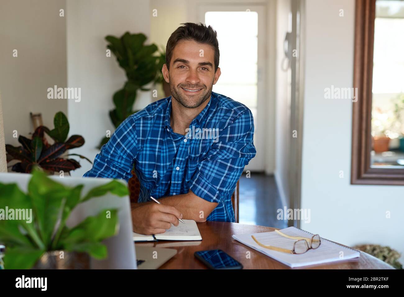 Lächelnder junger Mann, der von zu Hause aus in seinem Wohnzimmer arbeitet Stockfoto