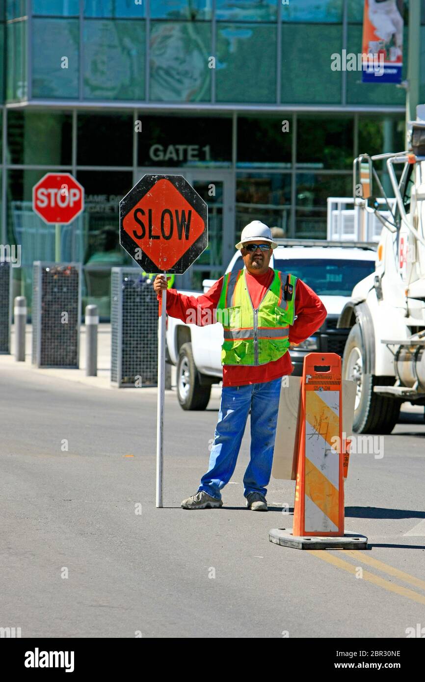 Der Verkehrskontroller steht auf der Straße mit einem "Slow"-Schild mit einem "Stopp"-Schild hinter ihm in Tucson AZ Stockfoto