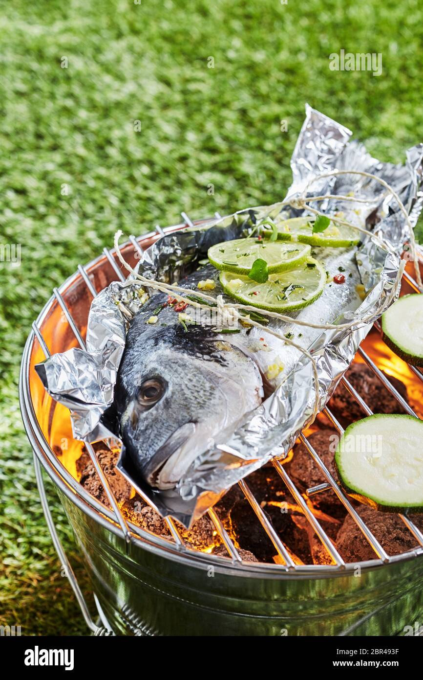 Ganz frischen, rohen Fisch grillen auf Alufolie über einem heißen Feuer im  Grill im Freien in einem Park oder Garten im Sommer Stockfotografie - Alamy