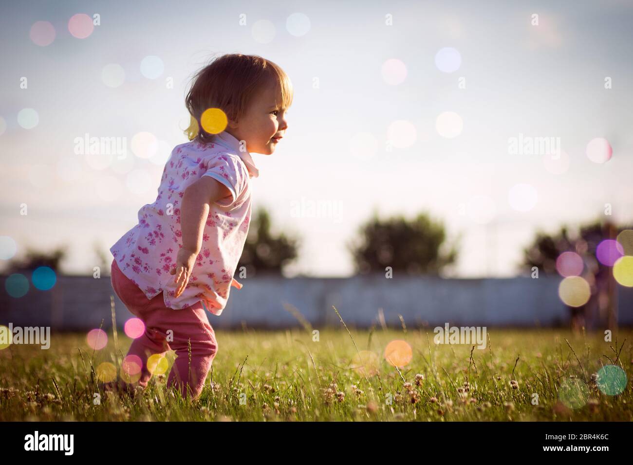 Ein Jahr alt oder 15 Monate alt verspielt Baby Mädchen spielt im Freien mit bunten Suppenblasen. Stockfoto