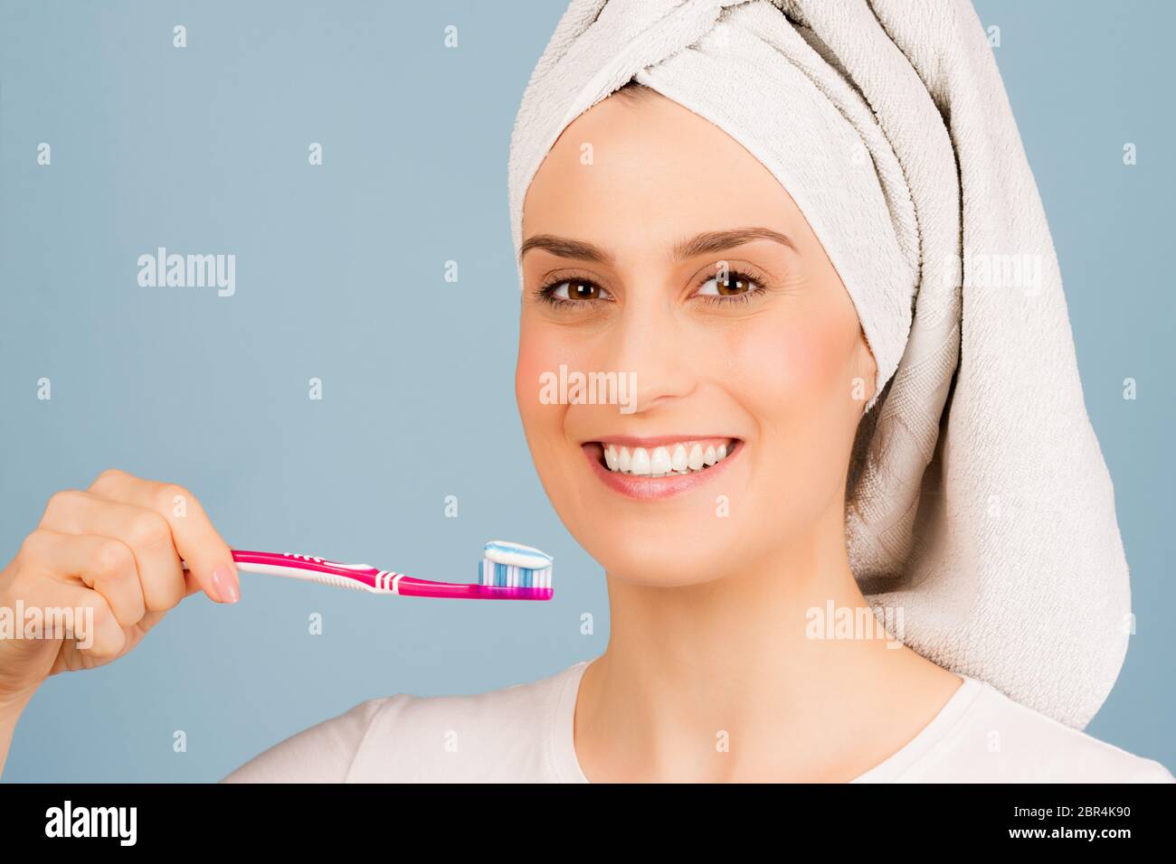 Die schöne lächelnde Frau mit weißem Handtuch auf dem Kopf ist bereit, Zähne auf hellblauem Hintergrund zu putzen. Stockfoto