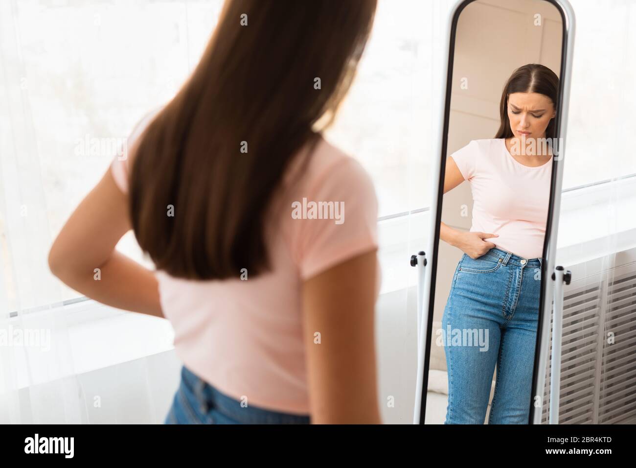 Unglückliche Frau Gewinnt An Gewicht Berühren Bauch Stehen Bei Mirror Indoors Stockfoto