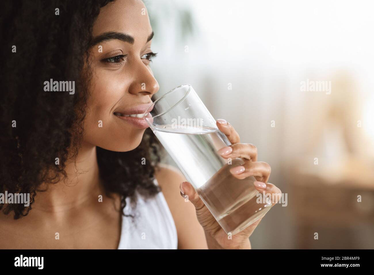 Gesunde Flüssigkeit. Lächelnde Schwarze Frau, Die Wasser Aus Glas Trinkt Und Wegschaut Stockfoto