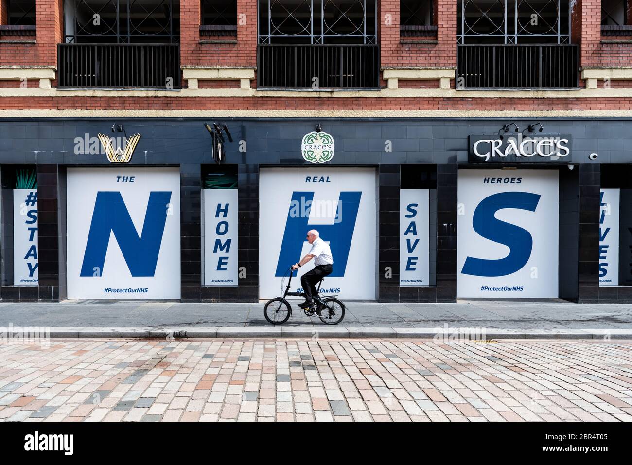 Glasgow, Schottland, Großbritannien. Mai 2020. Blockierung des Glasgow Coronavirus - ein älterer Radler passiert ein riesiges Schild "NHS Stay Home Save Lives" in den Fenstern eines geschlossenen Pubs im Stadtzentrum von Glasgow.Quelle: Kay Roxby/Alamy Live News Stockfoto