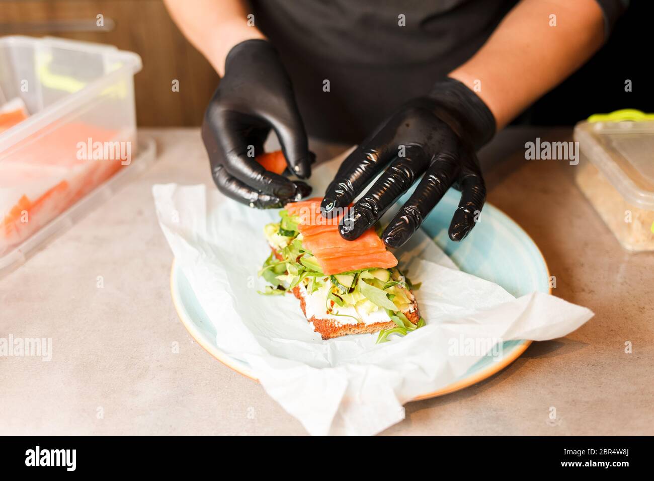 Kochen Sie die Hände Vorbereitung und Herstellung Sandwich. Zubereitung von gesunden vegetarischen Bruschettas in dunklen Handschuhen. Sandwich mit Weichkäse, Rucola, Gurke und SA Stockfoto