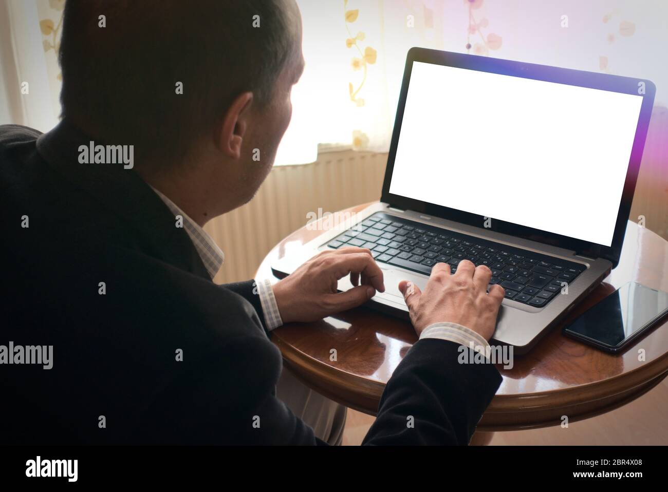 Senior Mann in Smart-Kleidung Browsen mit Laptop mit einem Telefon neben ihm auf einem Tisch zu Hause leeren Bildschirm kopieren Raum Stockfoto