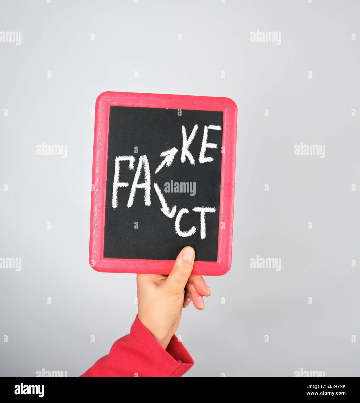 Weibliche Hand, die Kreide Rahmen mit Kreide Inschrift fake und tat, grauer Hintergrund Stockfoto