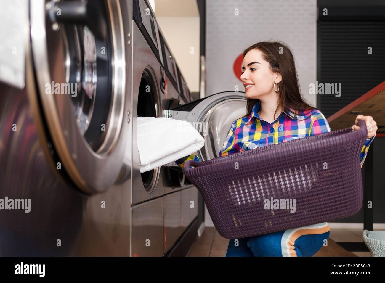 Mädchen lädt Wäsche in eine Waschmaschine. Frau in Waschküche Stockfoto