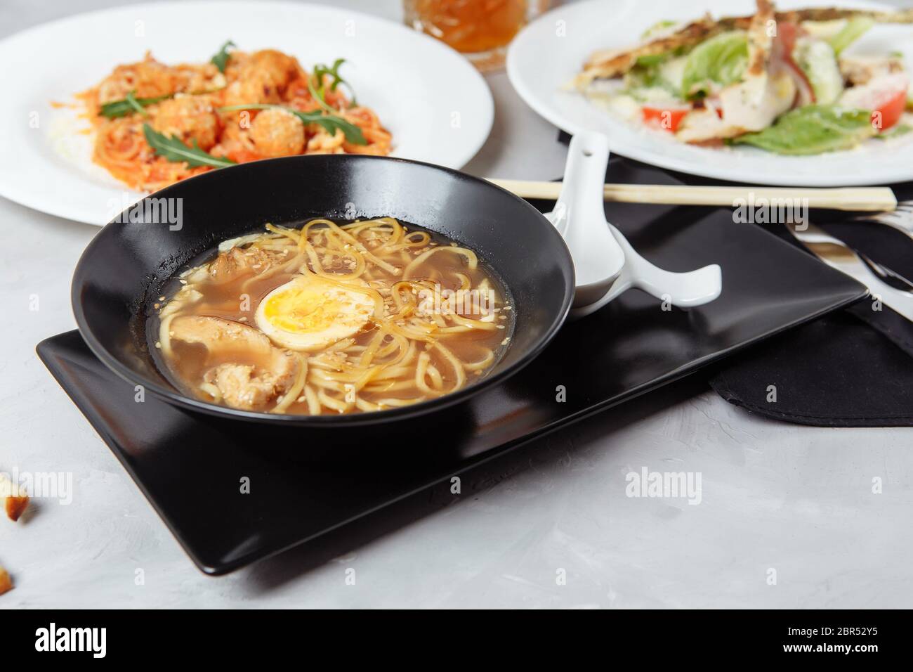 Drei-Gänge-Menü auf einem Tisch in einem Restaurant. Business Lunch von Bowl Ramen mit Huhn und Ei, frischem caesar Salat und Pasta Stockfoto