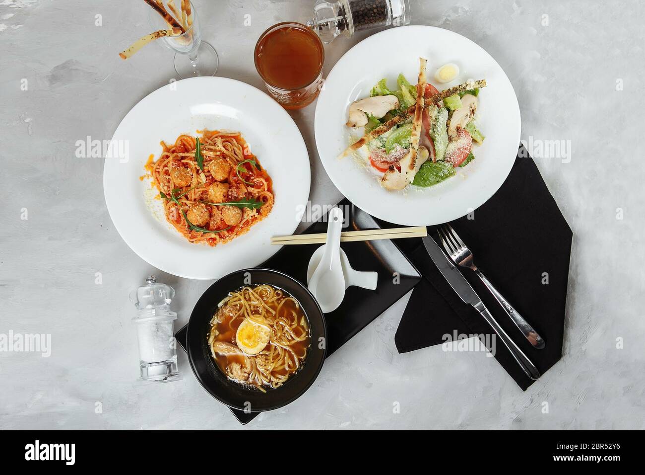 Drei-Gänge-Menü auf einem Tisch in einem Restaurant. Business Lunch von Bowl Ramen mit Huhn und Ei, frischem caesar Salat und Pasta Stockfoto