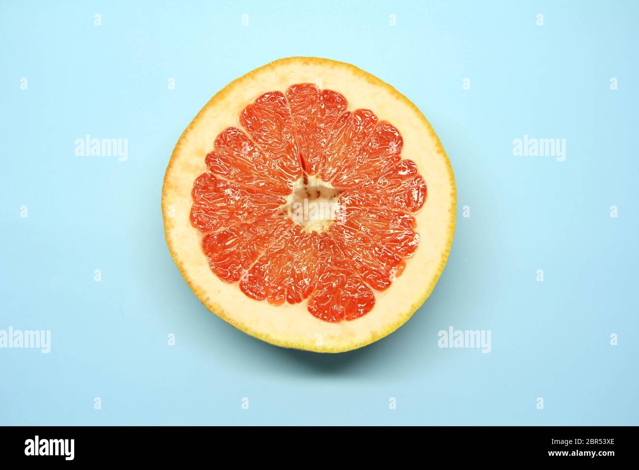 Eine halbe saftige rote Grapefruit. In Scheiben geschnittene aromatische Zitrusfrüchte auf blauem Hintergrund. Stockfoto