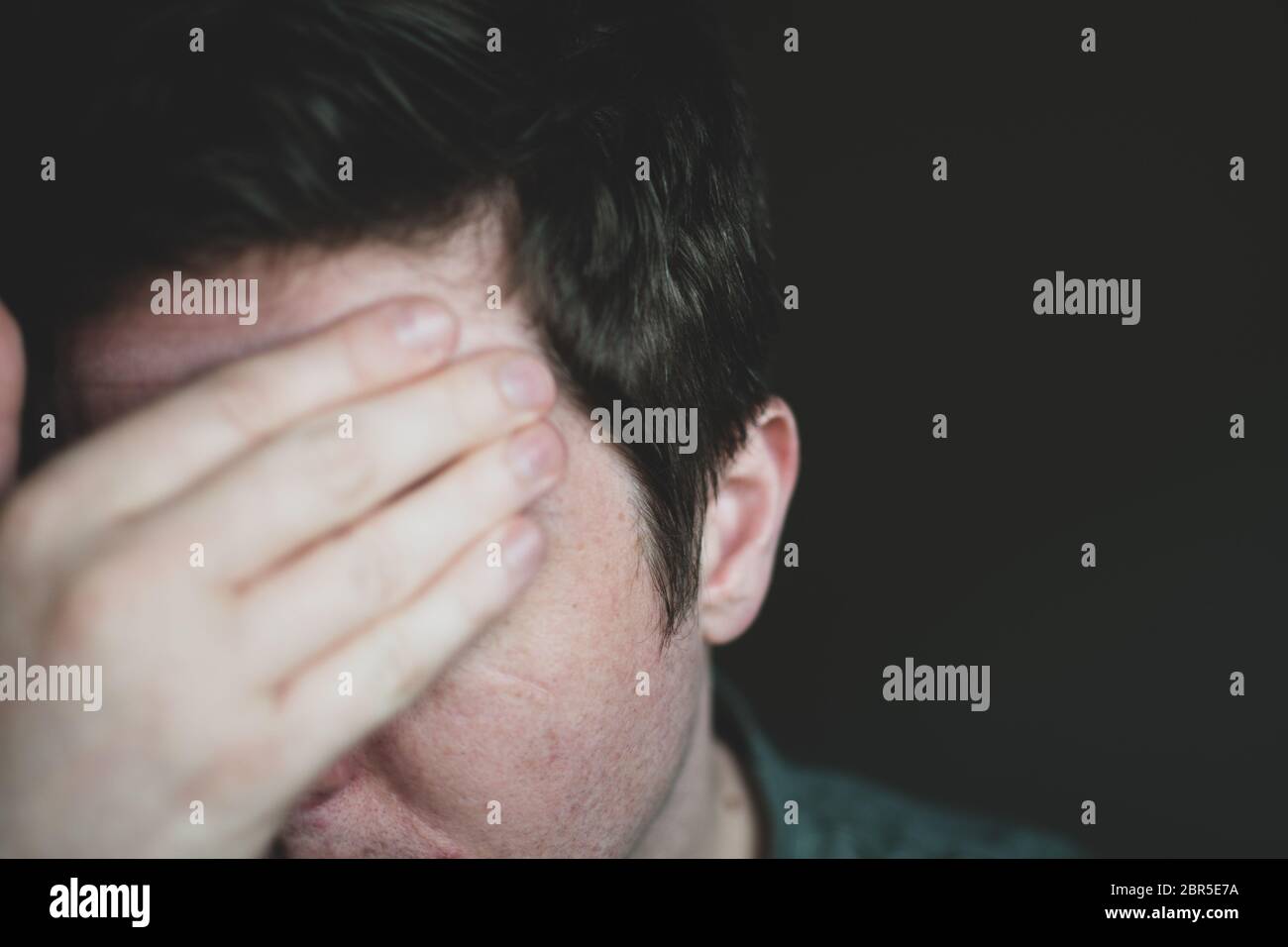 Ein erwachsener Rüde in den Dreißigern bedeckt sein Gesicht mit einer dunklen Hand. Stockfoto