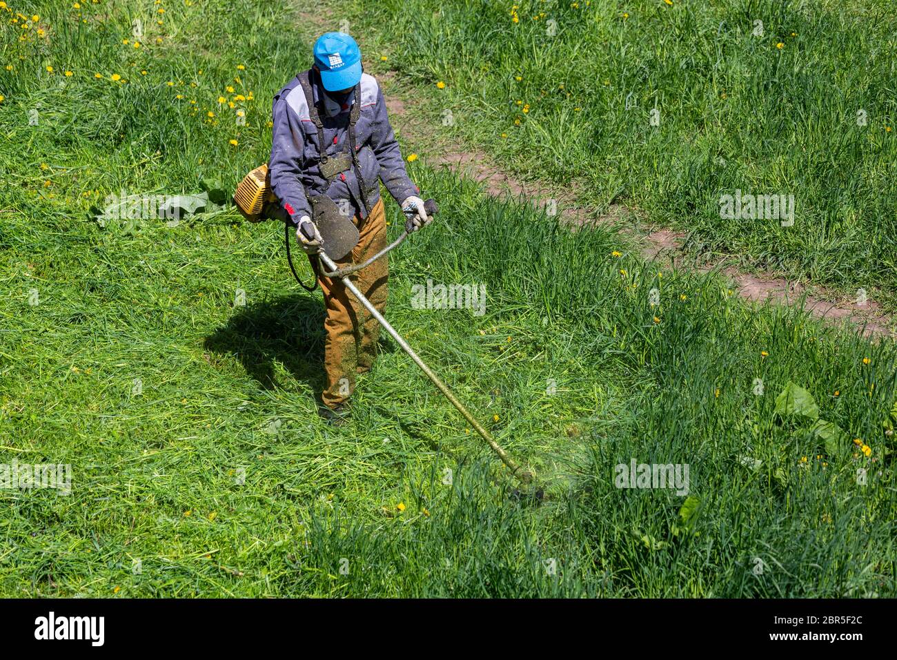 TULA, RUSSLAND - 19. MAI 2020: Russischer offizieller Rasenmäher Arbeiter Mann schneidet grünes Gras mit zwei-Zyklus-Motor-Saitentrimmer. Ansicht von oben nach unten. Stockfoto