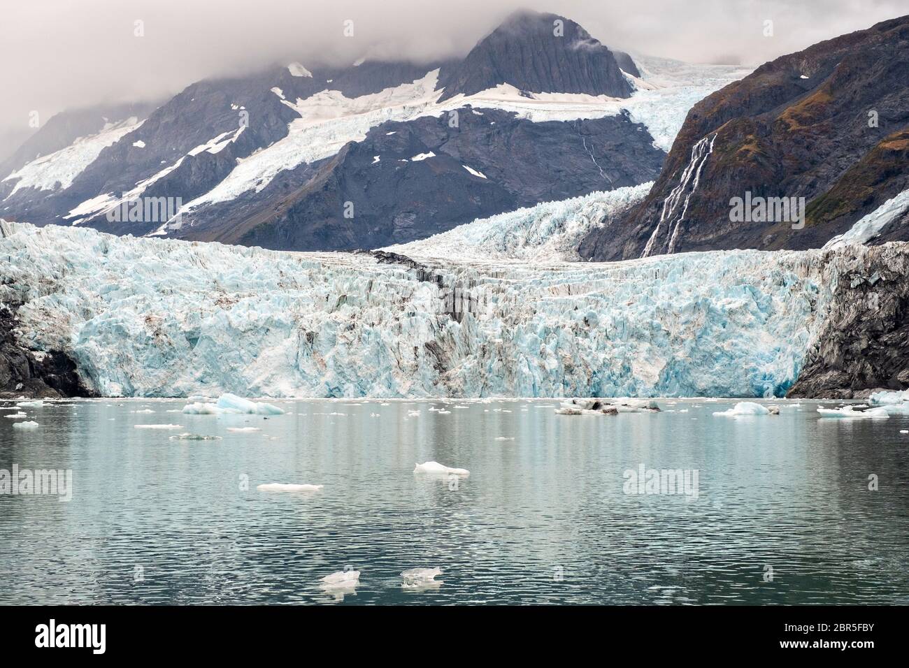 Der Überraschungsgletscher mit der mittleren Moräne und dem in Harriman Fjord in der Nähe von Whittier, Alaska schwimmenden Braseis. Surprise Glacier ist der aktivste kalbende Tauch-Gletscher im Prince William Sound. Stockfoto