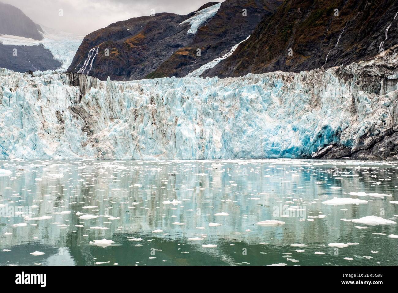 Der Überraschungsgletscher mit der mittleren Moräne und dem in Harriman Fjord in der Nähe von Whittier, Alaska schwimmenden Braseis. Surprise Glacier ist der aktivste kalbende Tauch-Gletscher im Prince William Sound. Stockfoto