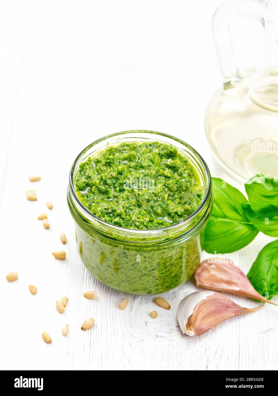 Pesto in einem Glas, Pinienkerne, Knoblauch, Basilikum und Olivenöl in eine Karaffe auf dem Hintergrund des Lichts Holzbrett Stockfoto