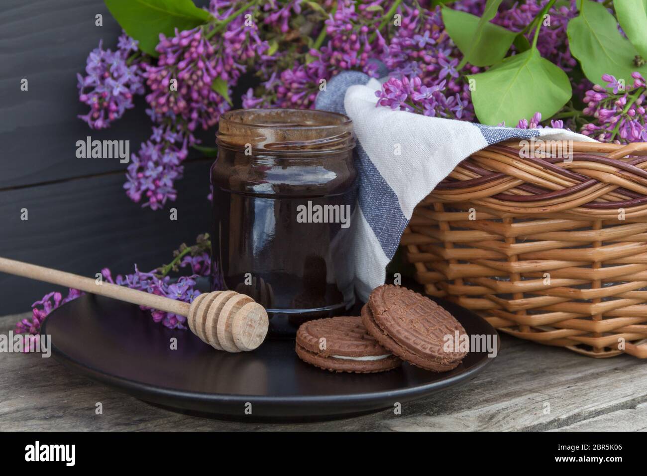 Ein Glas Honig oder Marmelade mit Korbkorb mit Flieder auf Holzhintergrund. Stockfoto