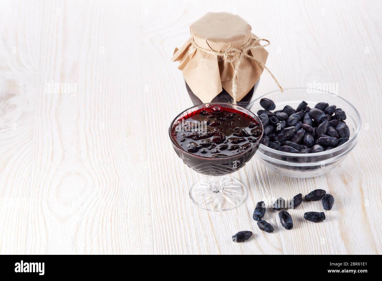 Geißblatt Beeren in einer Glasschüssel und Glas Marmelade stehen auf einem hölzernen Hintergrund. Stockfoto