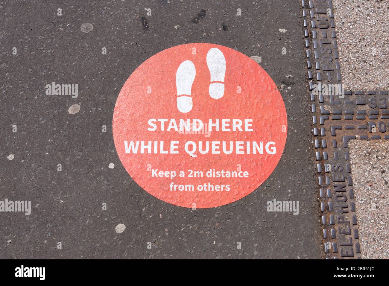 Social Distancing Queue Schild - Stehen Sie hier während der Coronavirus Pandemie auf dem Bürgersteig, während Sie sich in der Schlange anstellen Stockfoto