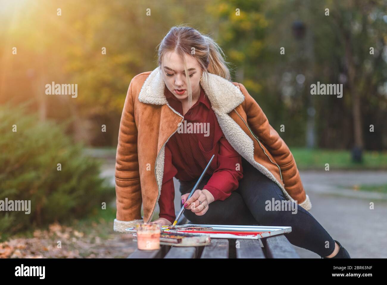 Der junge Maler zeichnet ein Bild, das in einem Park auf der Bank sitzt Stockfoto