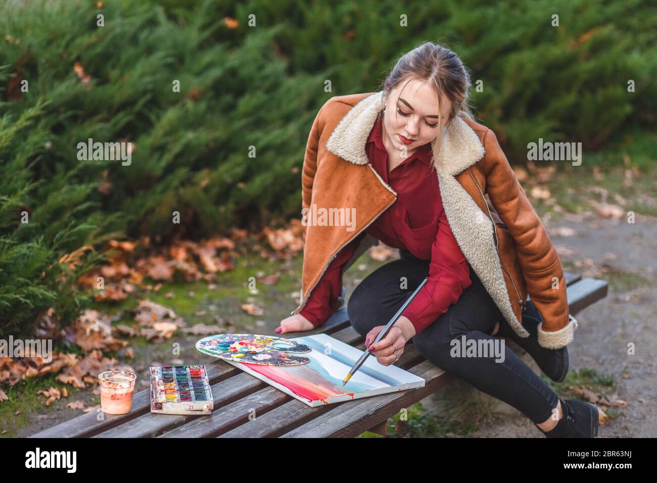 Der junge Maler zeichnet ein Bild, das in einem Park auf der Bank sitzt Stockfoto