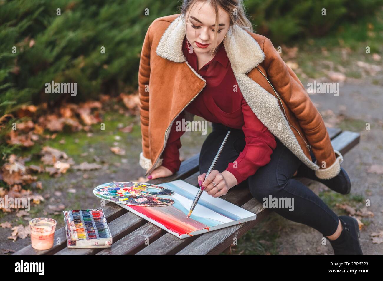 Der junge Maler zeichnet ein Bild, das in einem Park auf der Bank sitzt Stockfoto