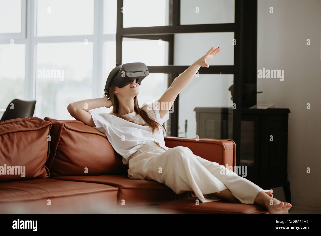Schöne junge Frau sitzt auf dem Sofa und berühren etwas mit Virtual Reality Headset Brille. Stockfoto