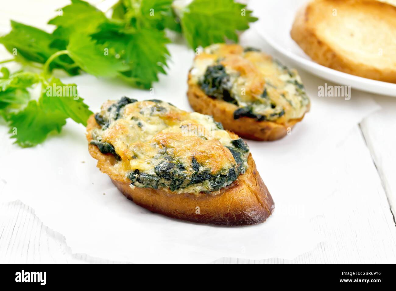 Warme Sandwiches mit Nesseln und Käse auf Scheiben Weizenbrot auf Pergament auf dem Hintergrund der Holzbretter Stockfoto