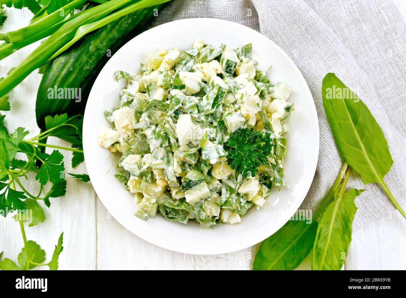 Salat aus Gurken, Sauerampfer, gekochte Kartoffeln, Eiern und Kräutern, mit Mayonnaise in eine weiße Platte, Petersilie, Frühlingszwiebeln und Serviette gegen die Bac gekleidet Stockfoto