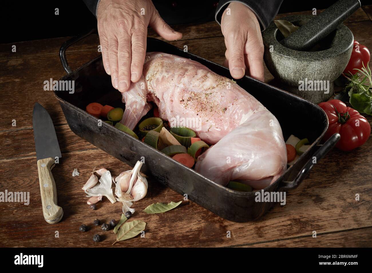 Der Küchenchef bereitet ein wildes Kaninchen für die Röstung reiben Gewürze auf das Fleisch in einen Bräter mit Lauch, Karotten, Tomaten Kräuter und Knoblauch Stockfoto