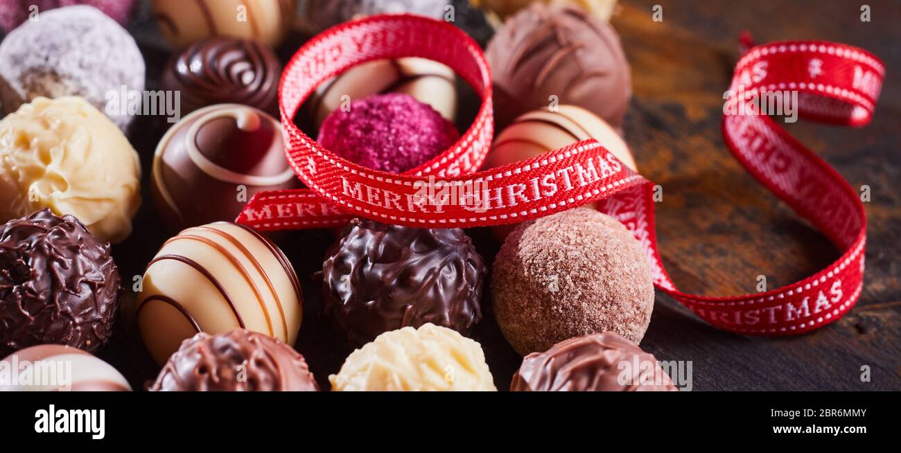 Rot festlich Frohe Weihnachten Band wirbelte über eine Auswahl an verschiedenen Gourmet handgefertigte Pralinen in Panorama banner Format Stockfoto