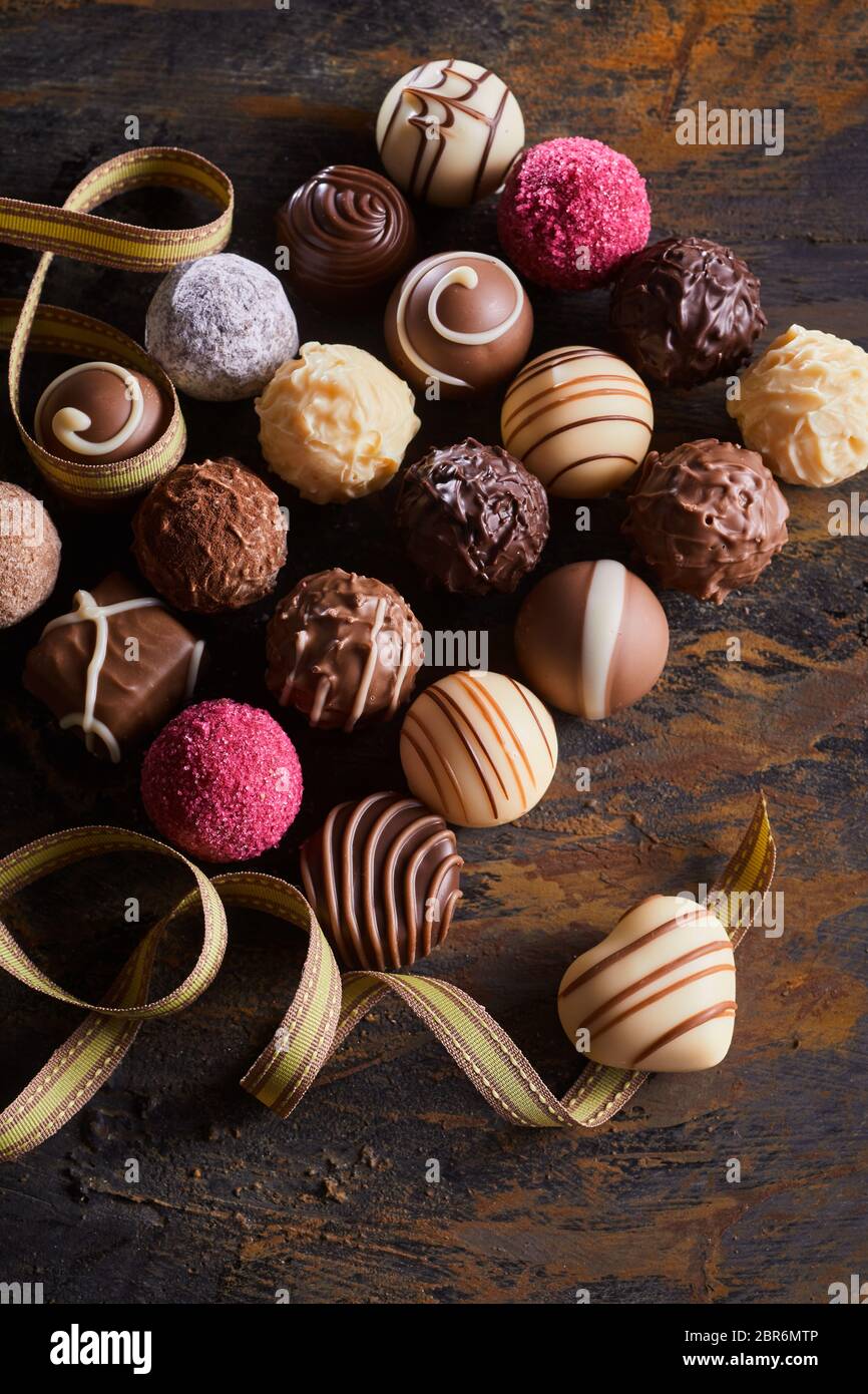 Valentines luxus Schokolade oder Pralinen Sortiment mit dekorativen handgemachte Pralinen und eine Zwirbelte Band mit einem Herzförmigen Schokolade hoch angesehen Stockfoto
