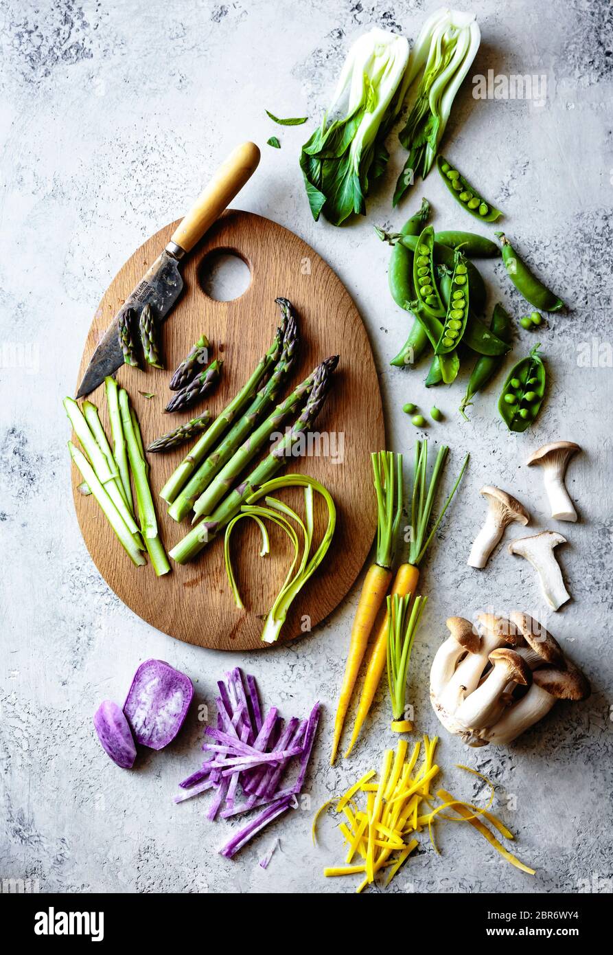 Spargel in Scheiben auf einem Holzbrett mit einer Auswahl an frischem, farbenfrohem Gemüse. Stockfoto