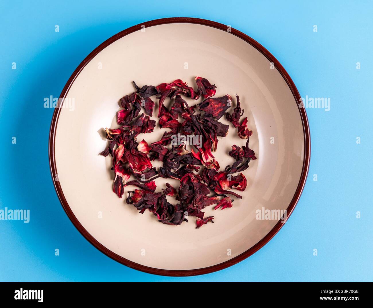 Haufen von trockenen Hibiskus Karkade Kräutertee auf einem Teller auf blauem Hintergrund, Draufsicht. Stockfoto