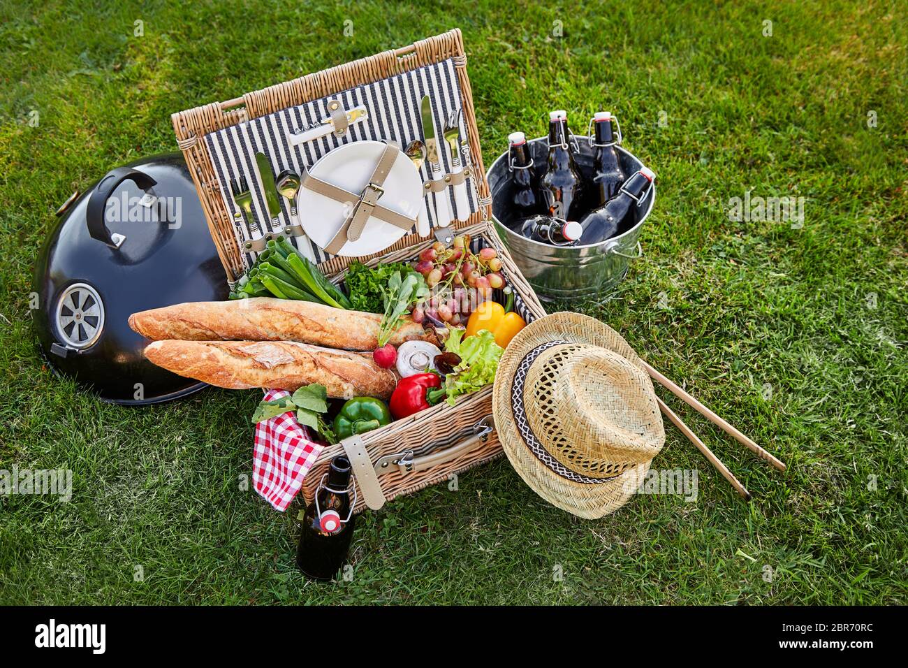 Vintage Style wicker Picknick mit frischem Gemüse für Salate und crusty französische Baguettes neben einem silbernen Kühler mit Flasche behindern Stockfoto