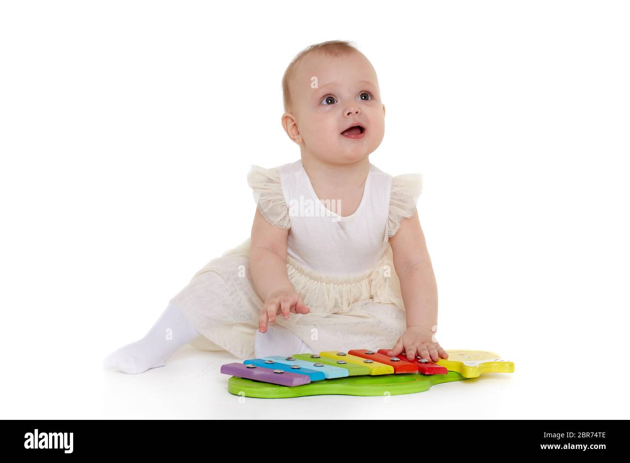 Süßes Baby im Kleid spielt mit buntem Xylophon (Musikinstrumentspielzeug für Kinder) auf weißem Hintergrund. Frühe Entwicklung und Lernspielzeug Stockfoto